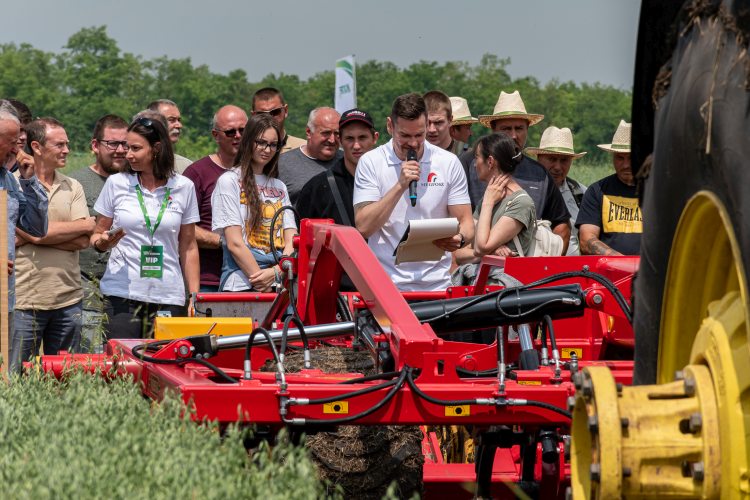 A fotón a NAK Szántóföldi Napok egyik szántóföldi gépbemutatója látható, ahol a résztvevők egy mezőgazdasági munkagépet figyelnek szakmai ismertetés közben.